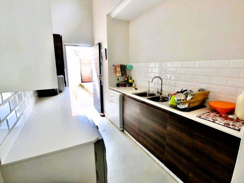 A functional scullery featuring modern dark wood cabinetry, white stone countertops, and a classic subway tile backsplash with a double basin sink.
