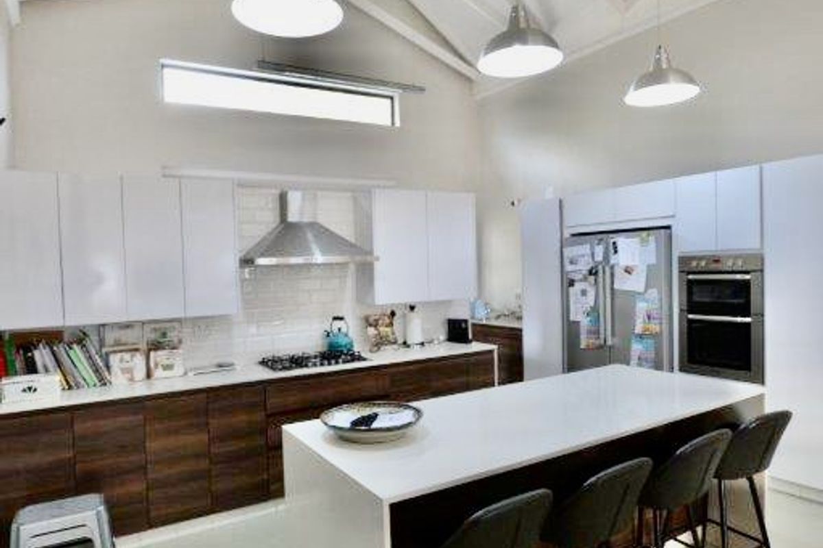 Modern kitchen featuring a large central island, high vaulted ceilings with exposed trusses, sleek cabinetry, and integrated appliances.