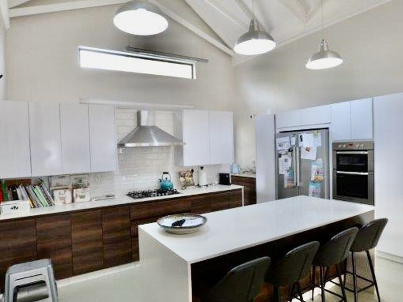Modern kitchen featuring a large central island, high vaulted ceilings with exposed trusses, sleek cabinetry, and integrated appliances.