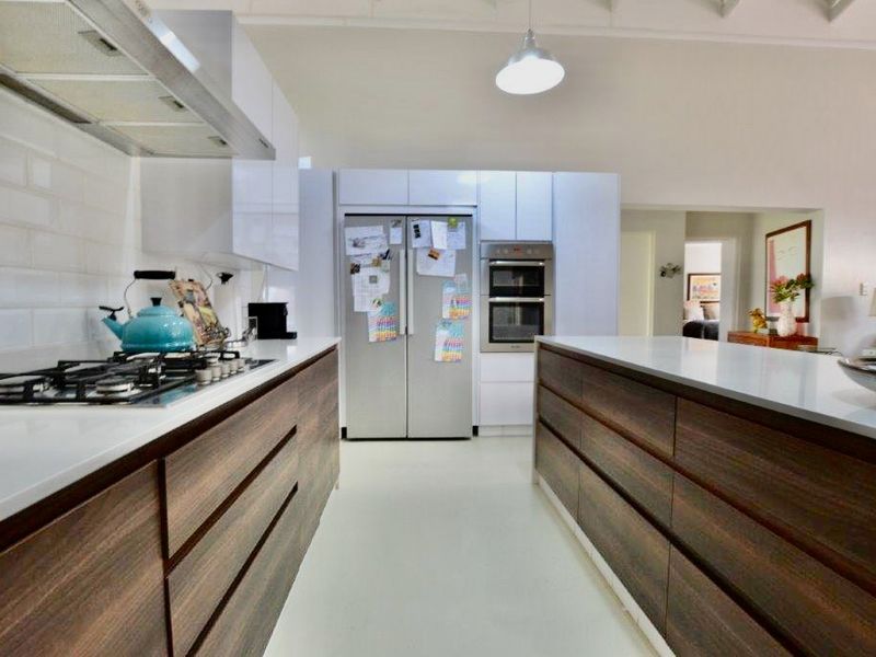 Modern kitchen featuring a central island, stone countertops, gas cooktop, built-in double oven, and sleek cabinetry with a subway tile backsplash.