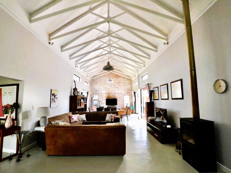 Spacious open-plan living area featuring a dramatic vaulted ceiling with exposed timber trusses, polished concrete floors, and a striking exposed brick feature wall.