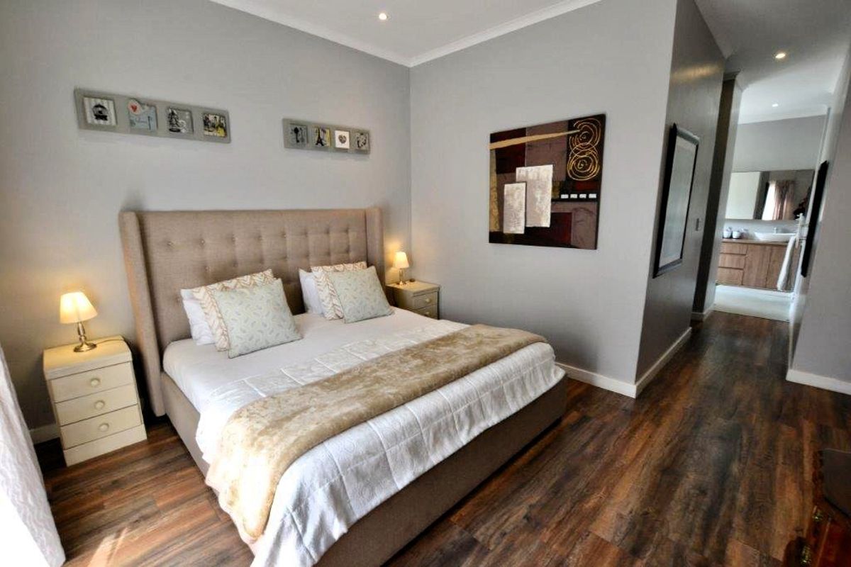 A well-maintained bedroom featuring modern laminate flooring, recessed downlighting, and an open-plan layout leading to an en-suite bathroom.