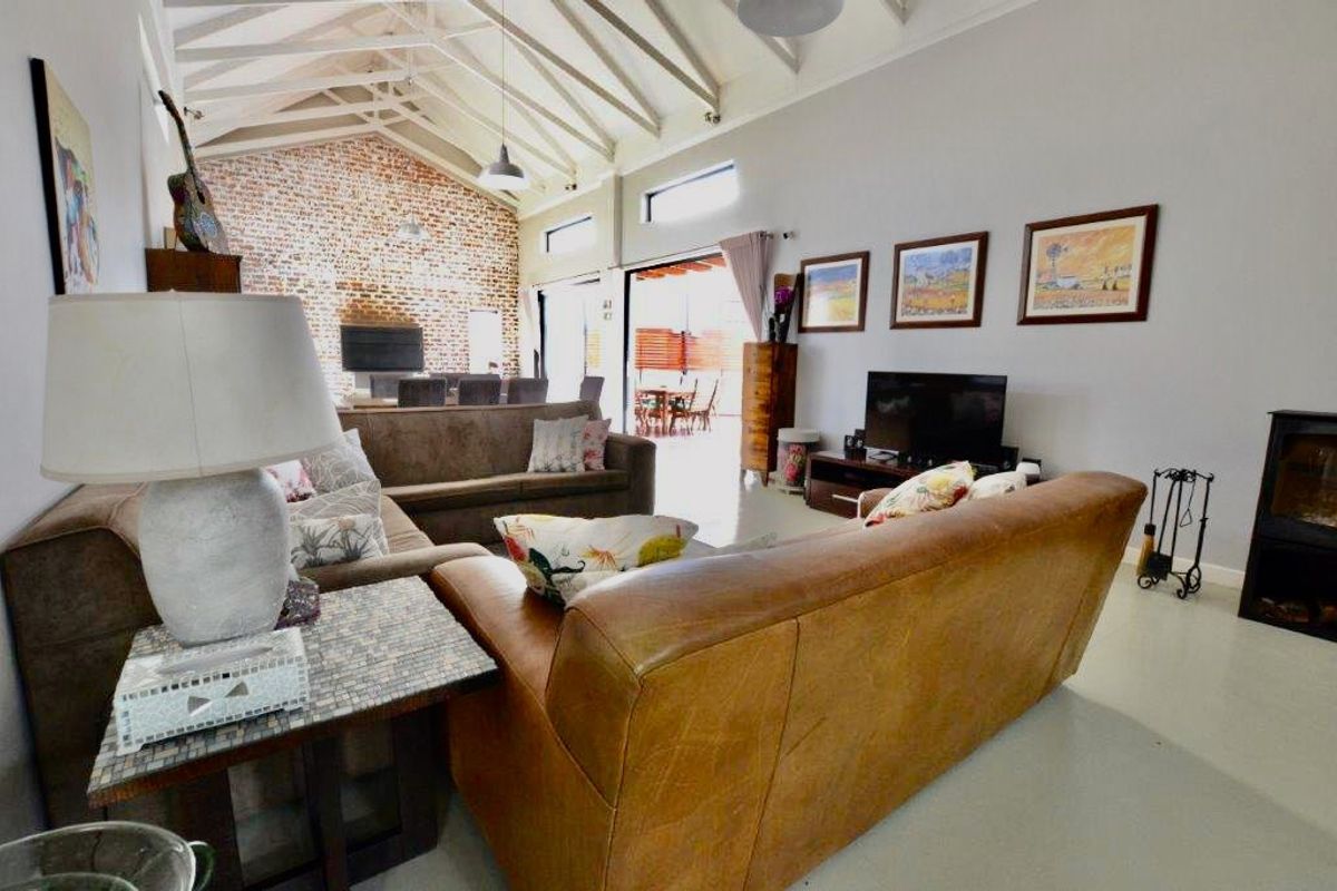 Spacious living room featuring a high vaulted ceiling with exposed rafters, an exposed brick feature wall, and a wood-burning stove.
