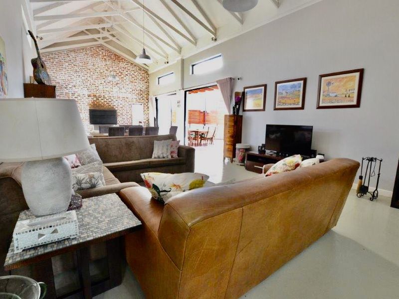 Spacious living room featuring a high vaulted ceiling with exposed rafters, an exposed brick feature wall, and a wood-burning stove.