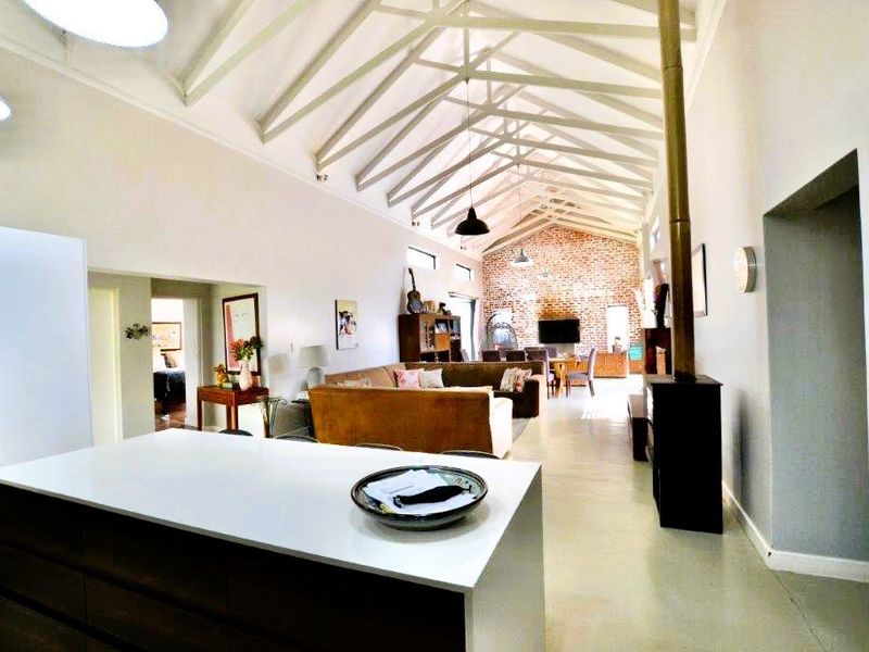 Spacious open-plan living area featuring high vaulted ceilings with exposed trusses, a striking brick feature wall, a modern kitchen island, and a cozy fireplace.