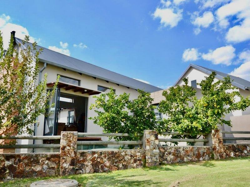 Rear view of the house featuring a stone boundary wall, timber fencing, and a covered patio area with sliding glass doors.
