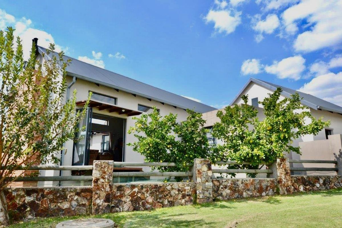 Rear view of the house featuring a stone boundary wall, timber fencing, and a covered patio area with sliding glass doors.