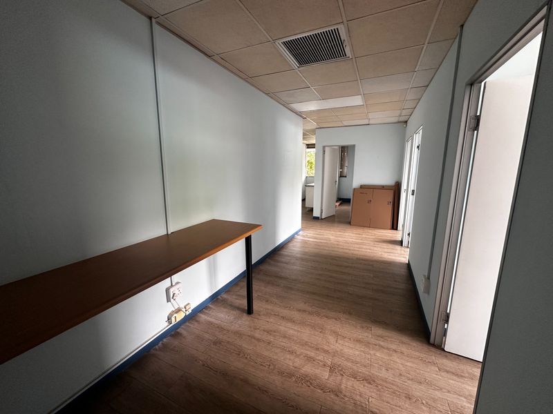 A functional commercial hallway featuring laminate flooring, a suspended ceiling with integrated air conditioning, and a built-in desk workspace.