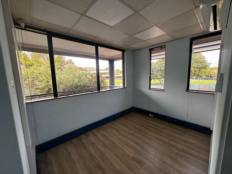 A bright, empty office space featuring laminate flooring, a suspended ceiling, and large windows providing natural light and views of the surrounding area.