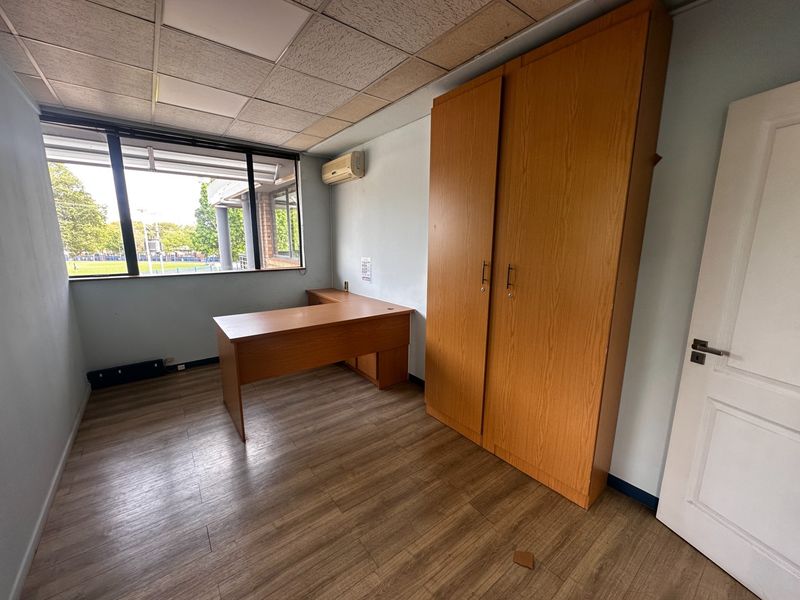 A functional office space featuring laminate flooring, a suspended ceiling, a split-system air conditioner, and large windows providing natural light.
