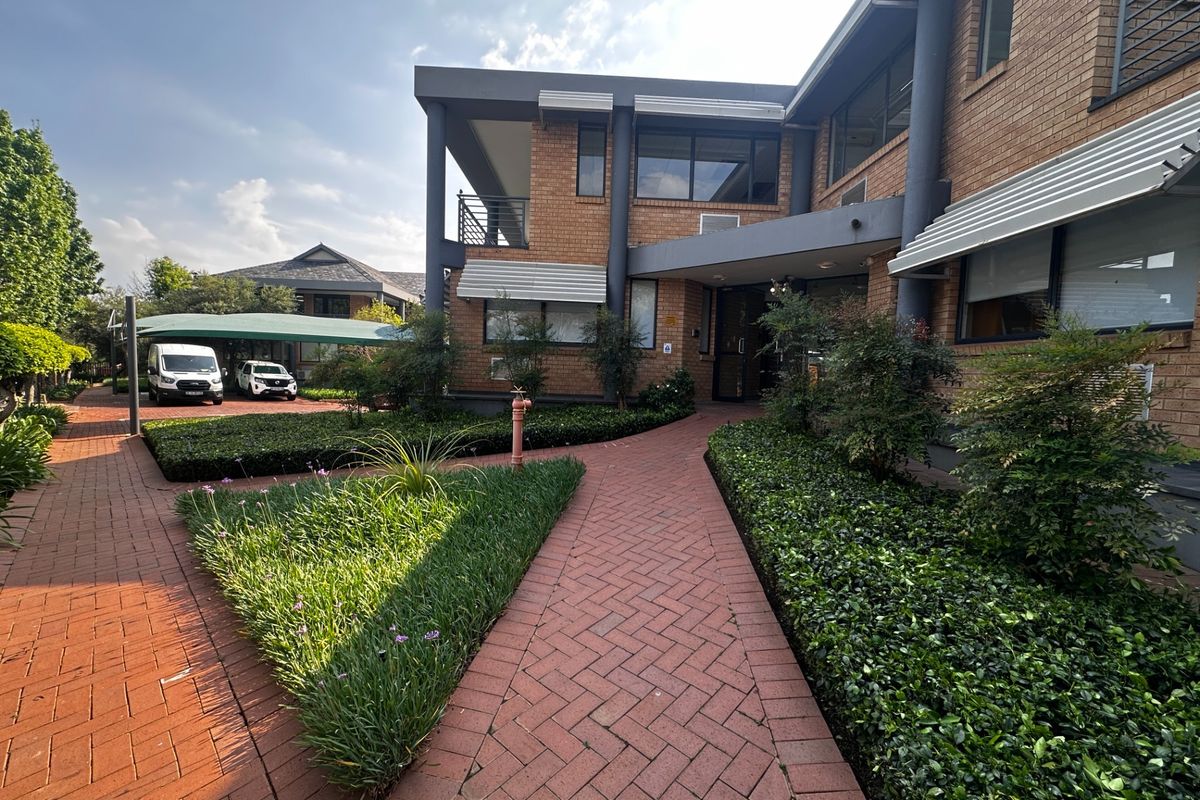 Front exterior view of a commercial brick building featuring a paved walkway, landscaped garden beds, and a covered parking area.