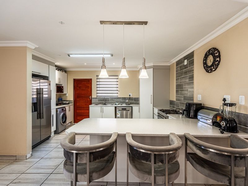 Modern kitchen featuring a central island with breakfast bar, stone countertops, tiled backsplash, integrated appliances, and contemporary pendant lighting.