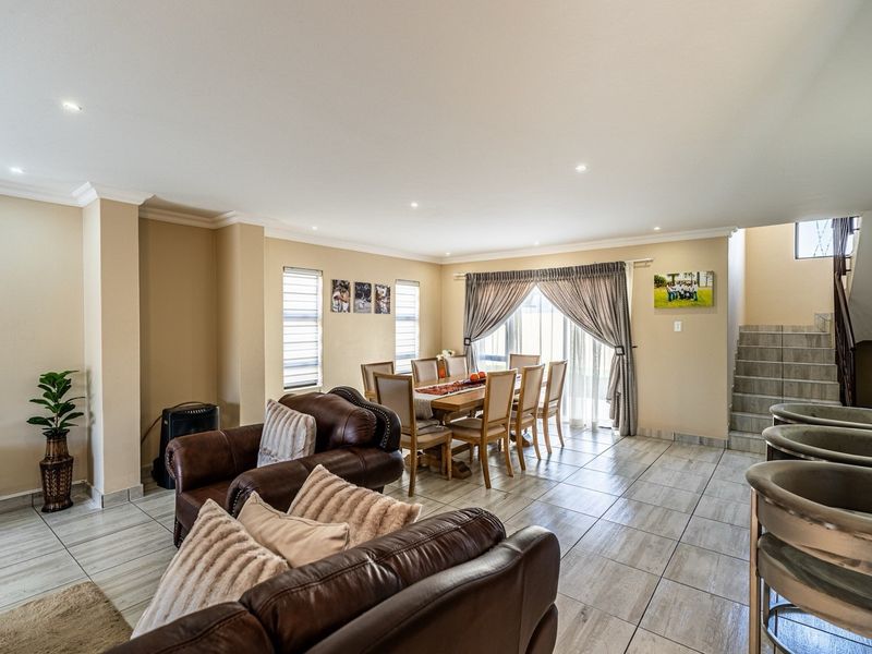 Spacious open-plan living and dining area featuring tiled flooring, recessed lighting, and a staircase leading to the upper level.