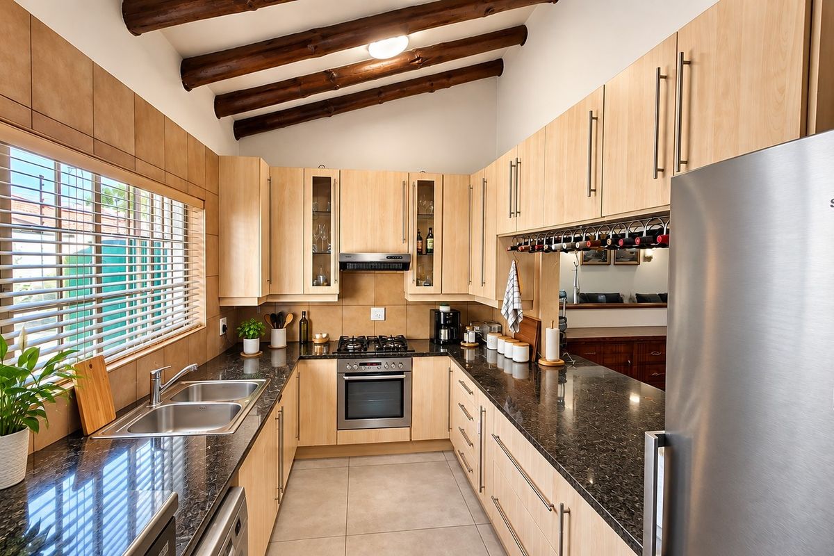 Modern kitchen featuring light wood cabinetry, granite countertops, double basin sink, gas hob, built-in oven, and distinctive exposed timber ceiling beams.