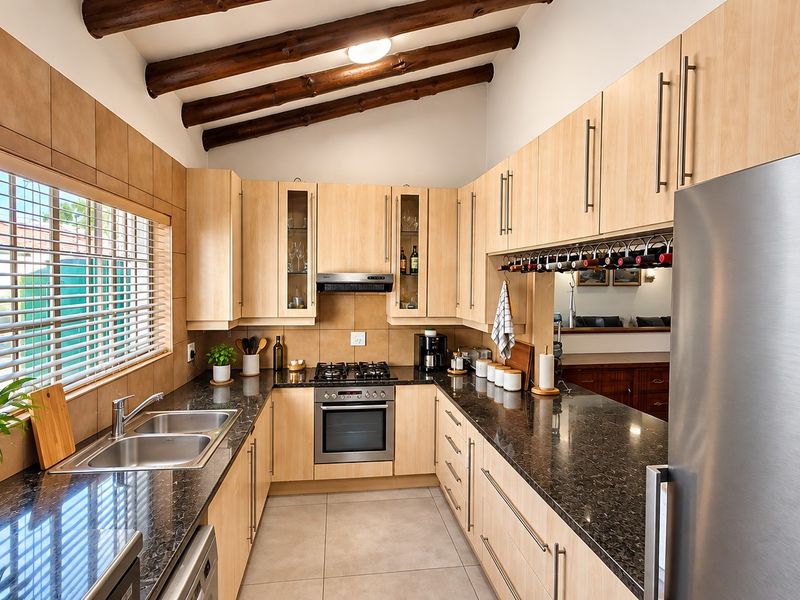 Modern kitchen featuring light wood cabinetry, granite countertops, double basin sink, gas hob, built-in oven, and distinctive exposed timber ceiling beams.