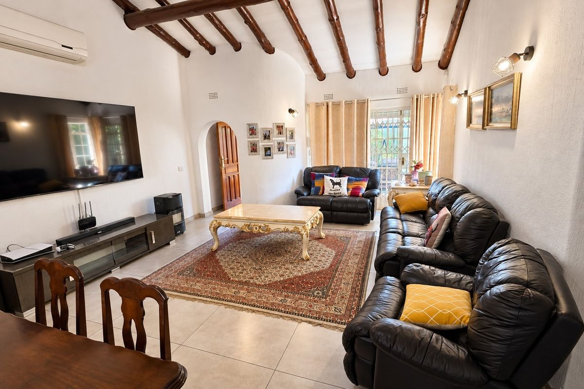 Spacious living room featuring exposed timber ceiling beams, tiled flooring, and an arched doorway leading to an outdoor area.