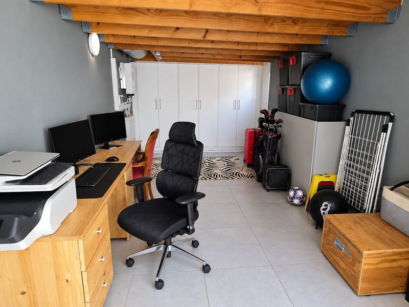 A functional home office space featuring tiled flooring, exposed timber ceiling beams, and ample built-in storage cabinetry.