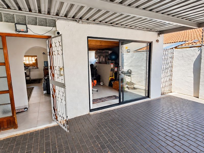 Covered patio area featuring brick paving, a security gate, and sliding glass doors providing access to the interior living space.