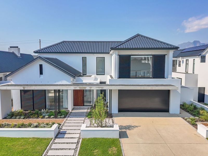 Modern double-story residential home featuring a sleek metal roof, double garage, paved driveway, and a well-maintained landscaped front garden.