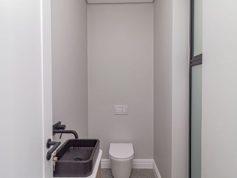 A modern, minimalist powder room featuring a wall-hung toilet with a concealed cistern and a contemporary black vessel sink with wall-mounted tapware.