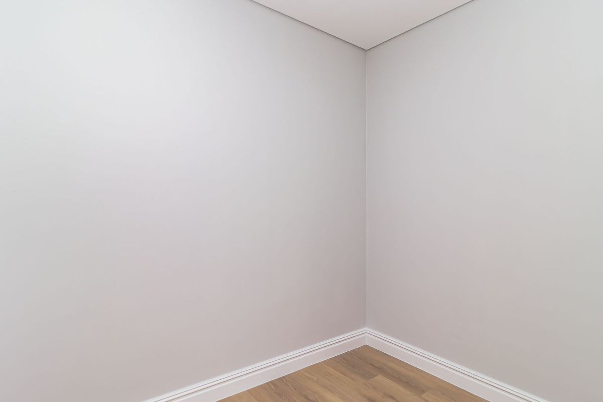 A clean, empty room corner featuring neutral grey walls, modern laminate flooring, and crisp white skirting boards.