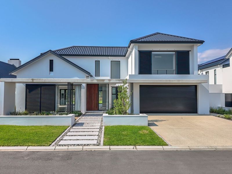 Modern double-story residence featuring a sleek white facade, dark metal roof, integrated double garage, and a landscaped front garden with a stone-paved entrance path.