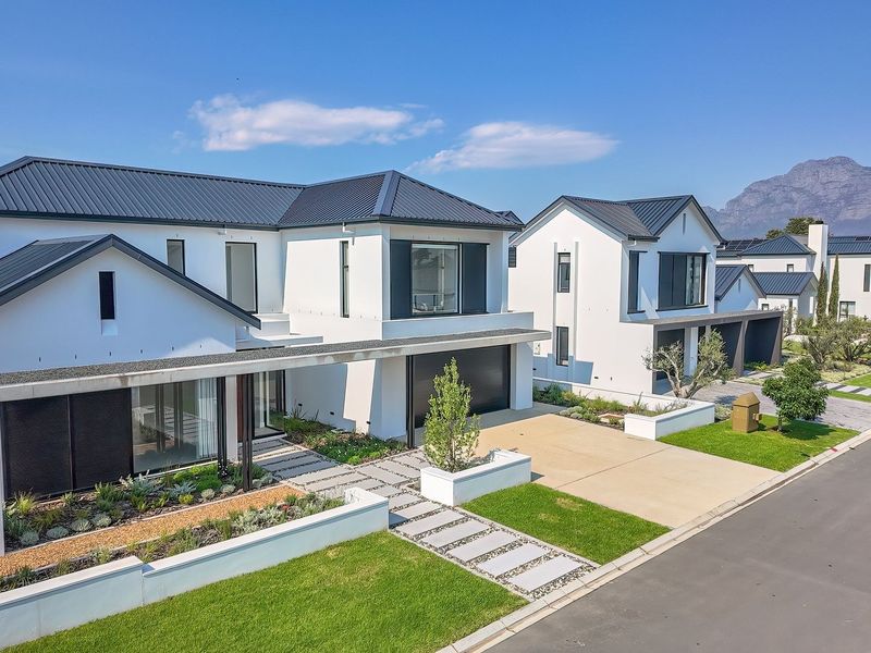 Modern contemporary residential property featuring a sleek metal roof, paved driveway, and manicured landscaping in a well-maintained estate setting.