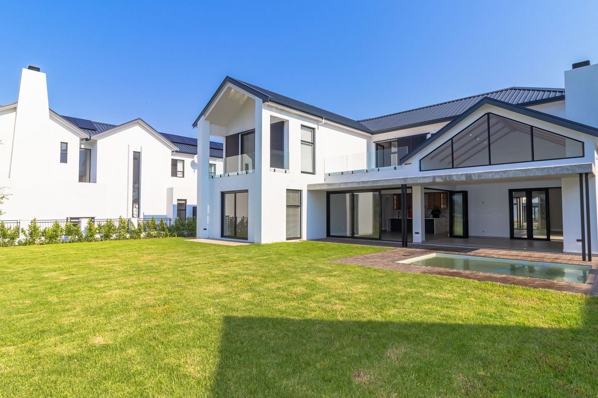 Modern rear elevation featuring a spacious lawn, swimming pool, covered patio, and contemporary architectural design with large glass sliding doors.