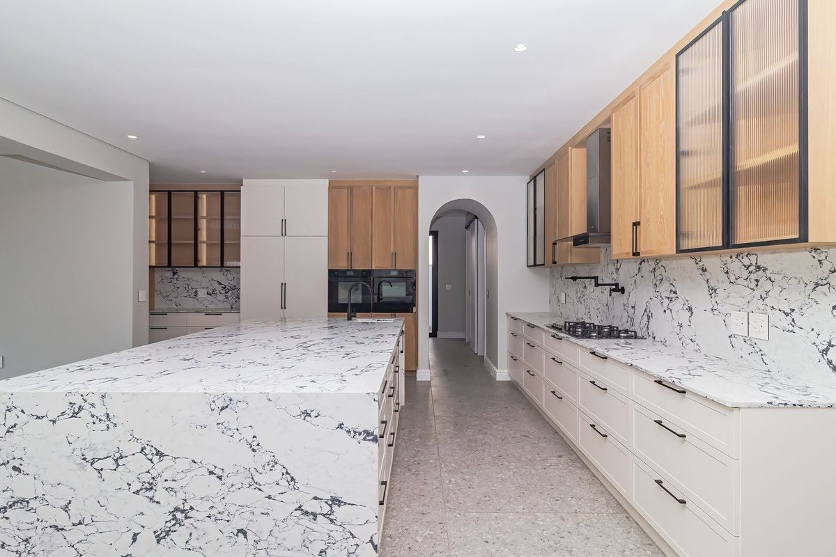 Modern kitchen featuring a large marble waterfall island, marble backsplash, high-end built-in appliances, and elegant shaker-style cabinetry with fluted glass accents.