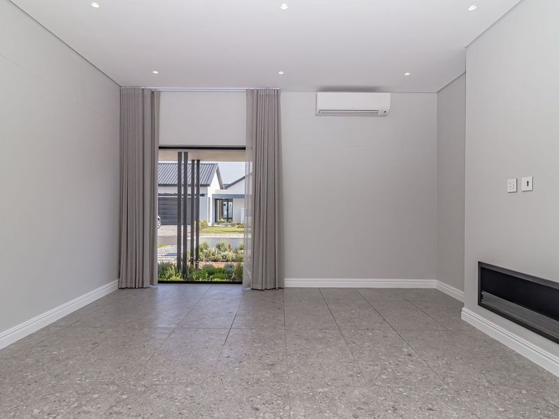 A bright, empty living room featuring modern tiled flooring, a built-in fireplace, and a wall-mounted air conditioning unit with access to the exterior.
