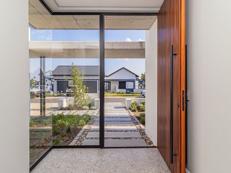 Modern entrance featuring a large timber pivot door, floor-to-ceiling glass panels, exposed concrete ceiling, and stone tile flooring with a view of the driveway.