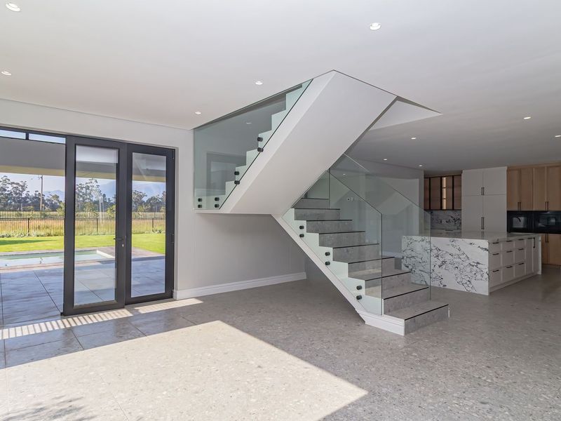 Spacious open-plan living area featuring a modern glass-railed staircase, marble-topped kitchen island, and seamless access to the outdoor patio and pool area.