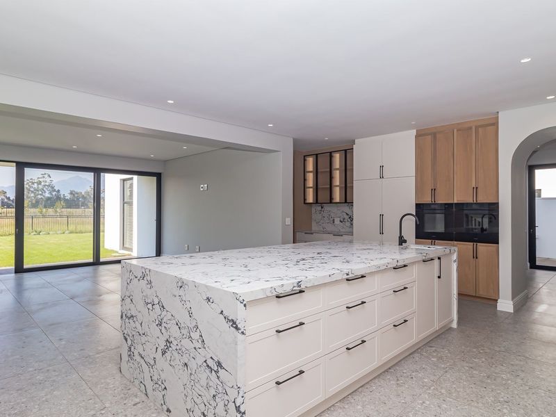 Modern open-plan kitchen and living area featuring a large marble-look island, sleek cabinetry, and expansive sliding doors leading to the garden.