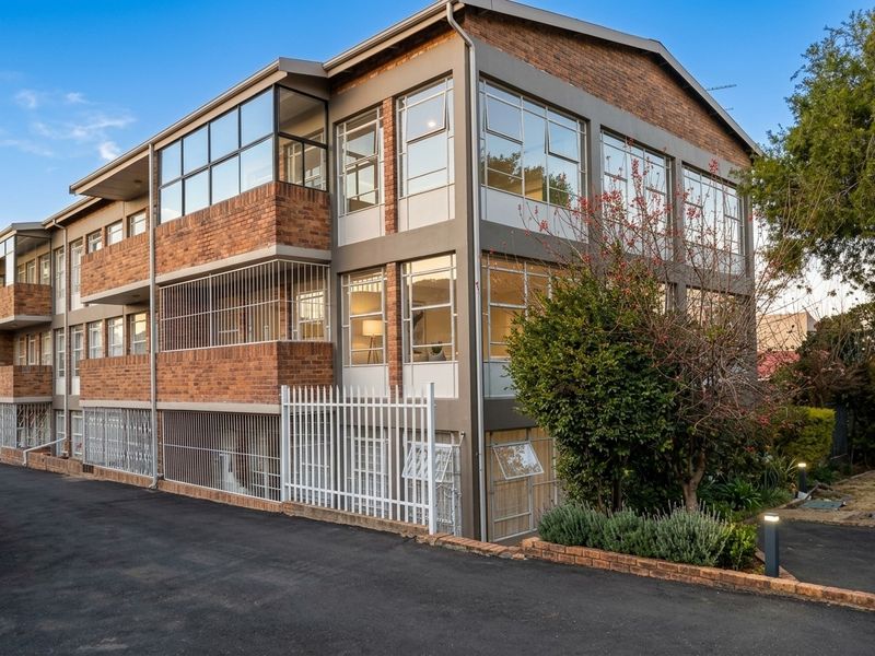 Exterior view of a multi-story apartment building featuring brick masonry, large windows, and secure ground-level metal fencing.