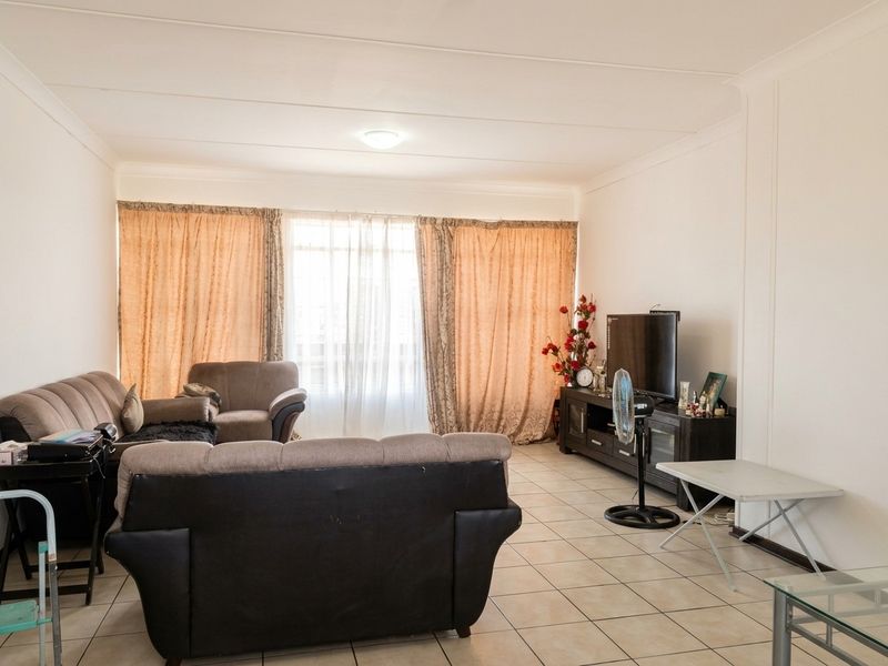 A spacious living room featuring neutral tiled flooring and large windows with curtains, providing a functional and well-lit area for relaxation.