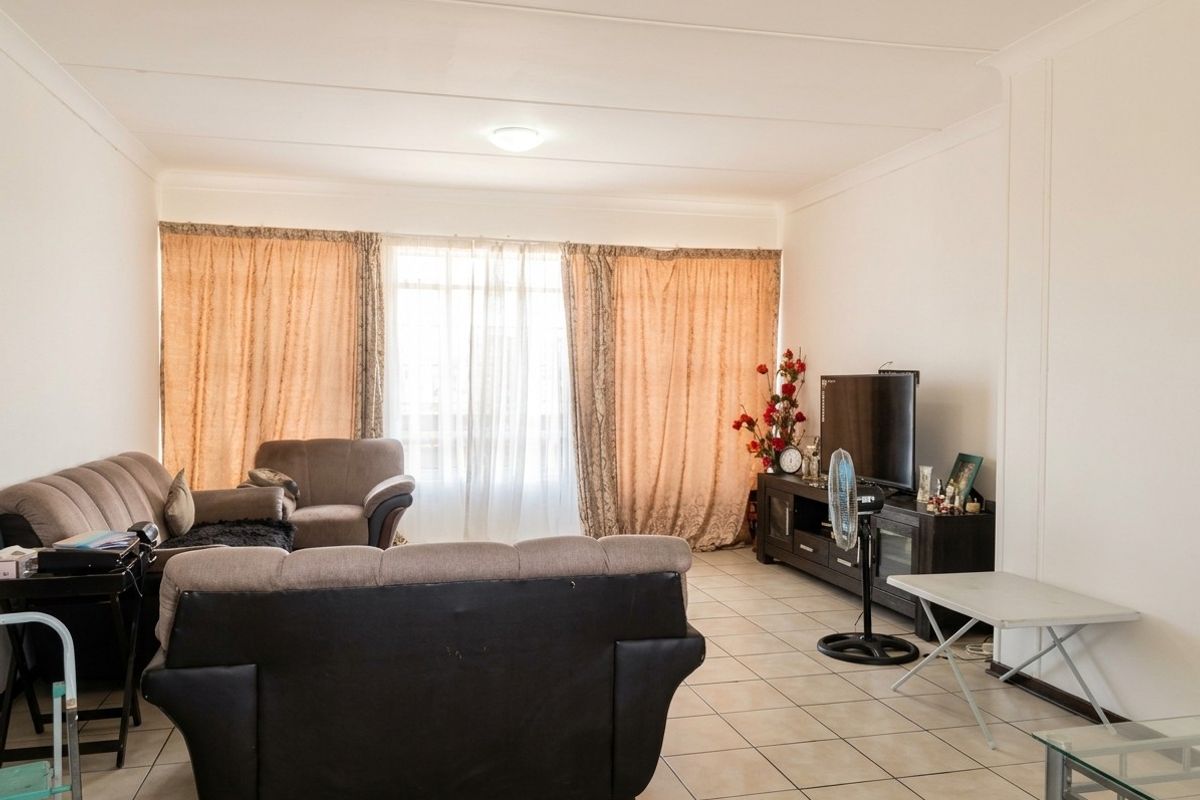 A spacious living room featuring neutral tiled flooring and large windows with curtains, providing a functional and well-lit area for relaxation.