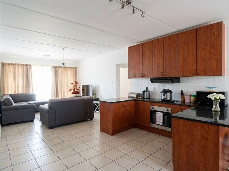 Open-plan living area featuring a kitchen with wood-finish cabinetry, granite countertops, built-in oven, and tiled flooring throughout the combined space.