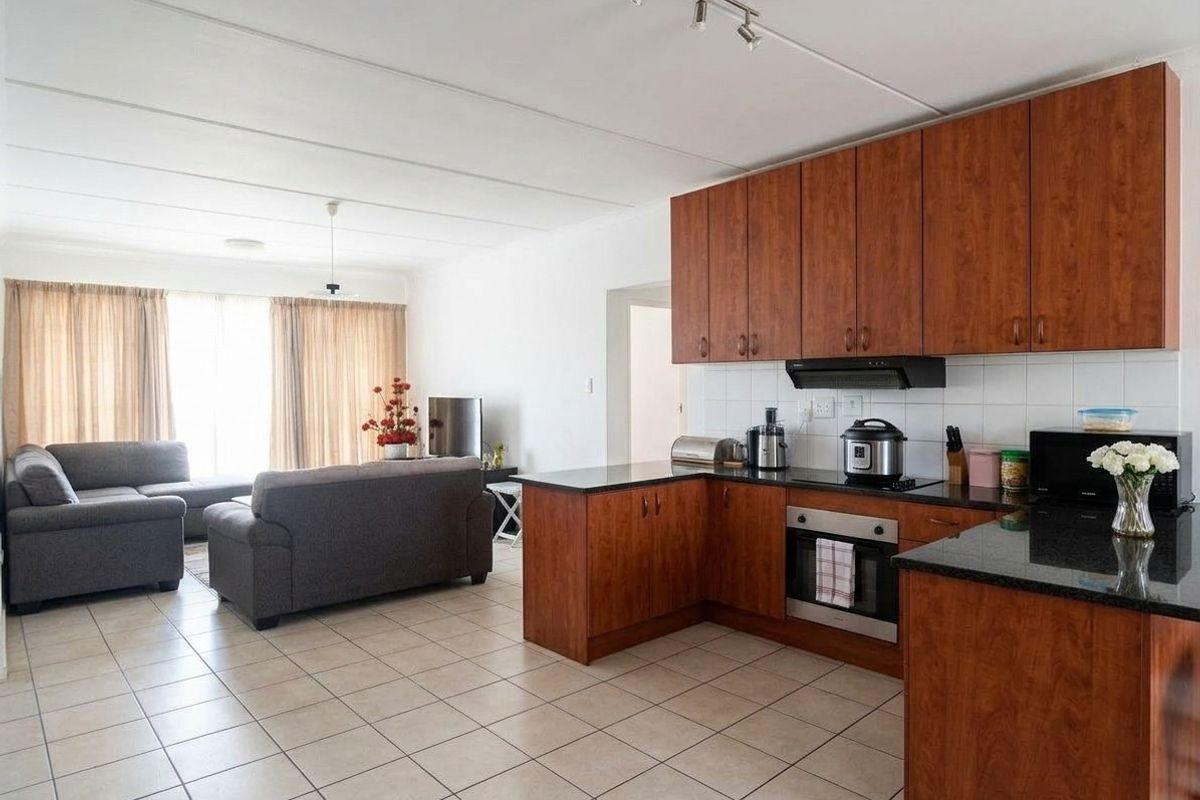 Open-plan living area featuring a kitchen with wood-finish cabinetry, granite countertops, built-in oven, and tiled flooring throughout the combined space.