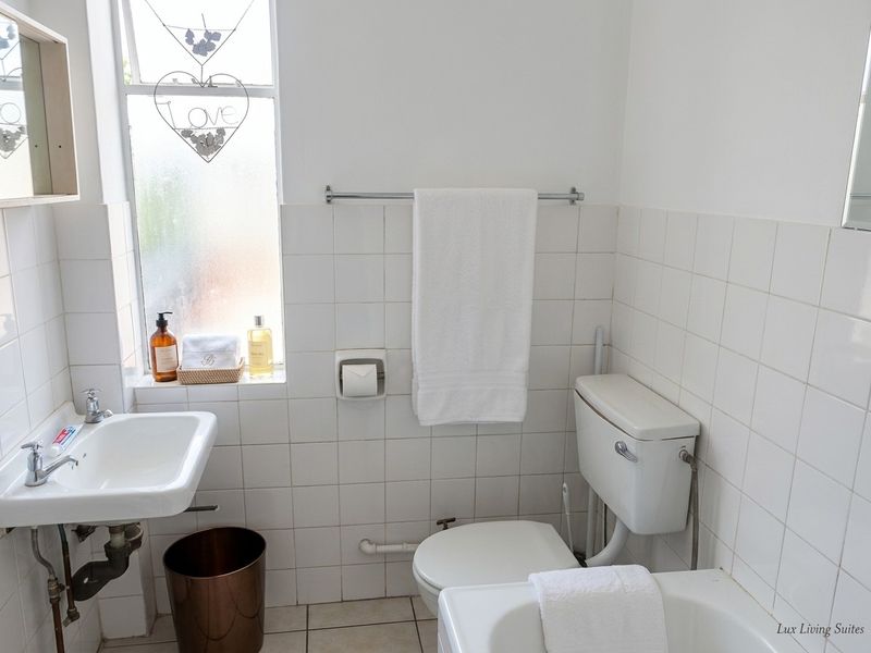 A functional bathroom featuring white wall tiles, a wall-mounted basin, and a standard toilet with a frosted window for natural light.