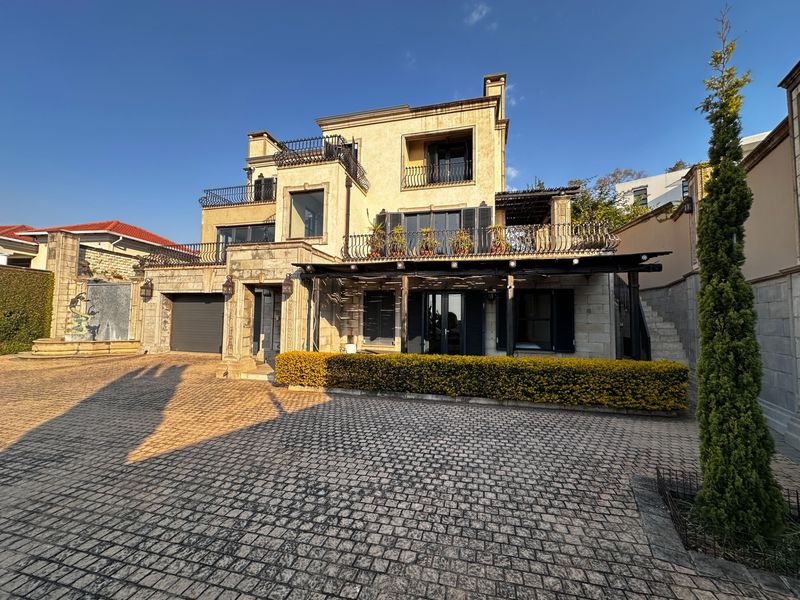 A multi-story stone residence featuring a cobblestone driveway, wrought iron balcony railings, a covered patio, and an integrated garage.