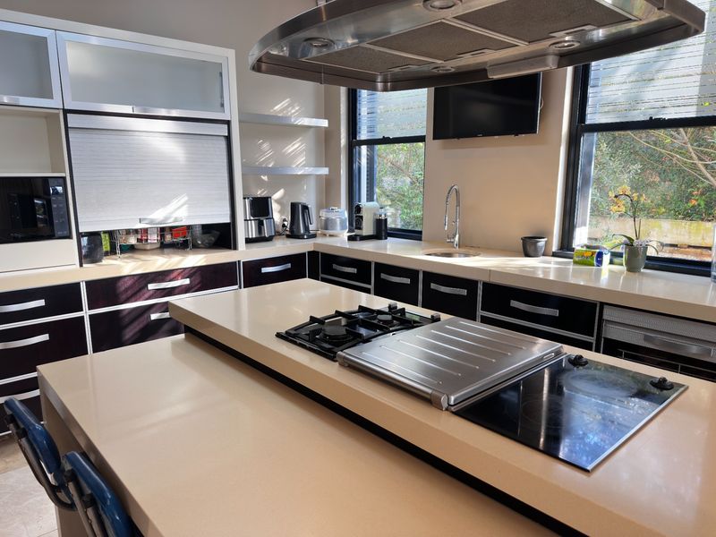 Modern kitchen featuring a large central island with dual cooktops, stone countertops, integrated cabinetry, and a stainless steel extractor fan.