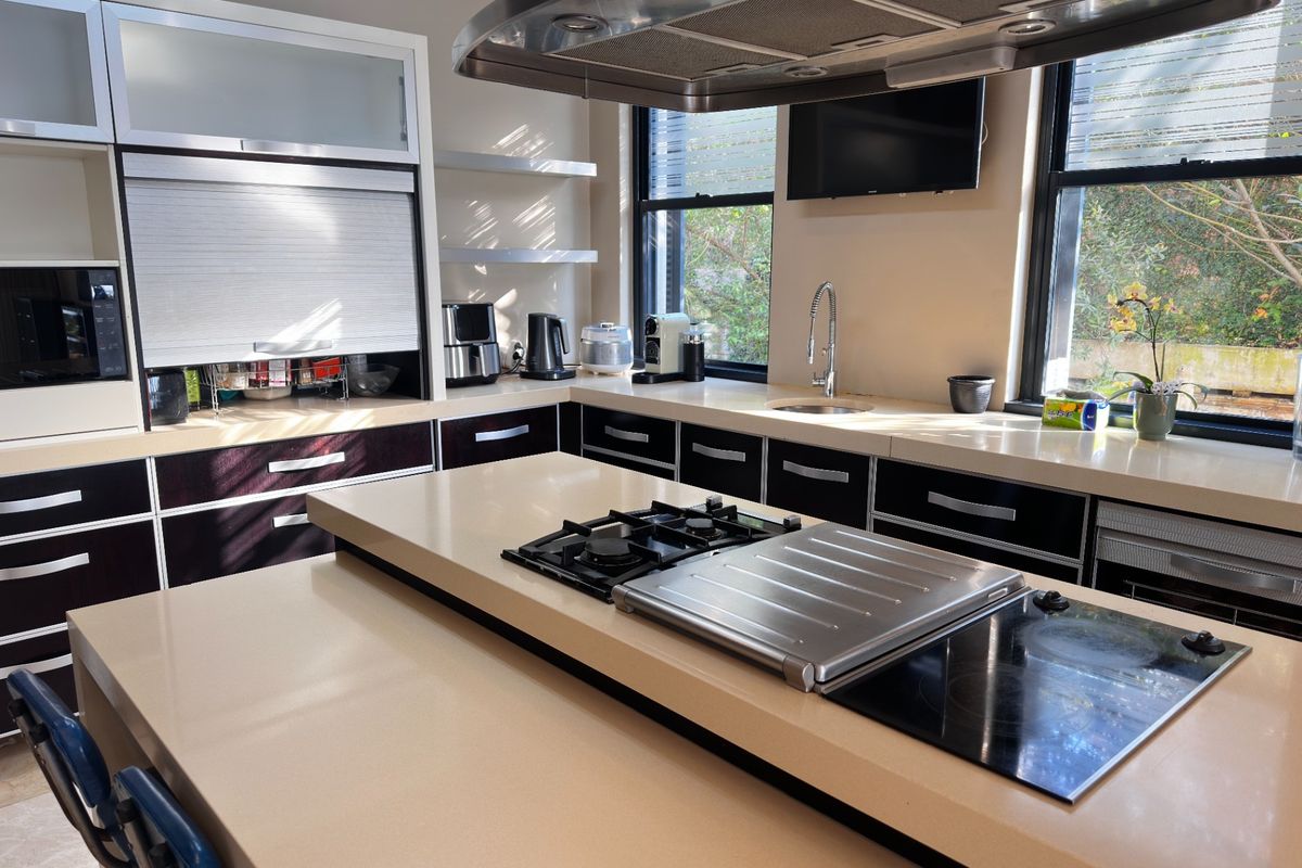 Modern kitchen featuring a large central island with dual cooktops, stone countertops, integrated cabinetry, and a stainless steel extractor fan.