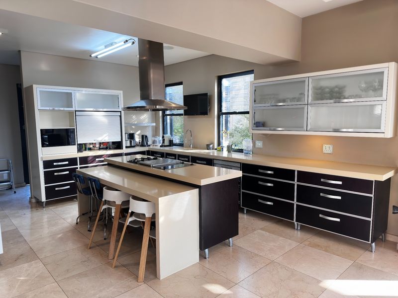Modern kitchen featuring a central island with integrated cooktop, stainless steel extractor fan, stone countertops, and ample dark-toned cabinetry with glass-fronted upper units.
