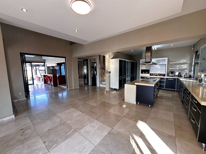 Spacious open-plan kitchen featuring a large central island, modern cabinetry, stone countertops, and seamless flow to an outdoor patio area through bi-fold doors.
