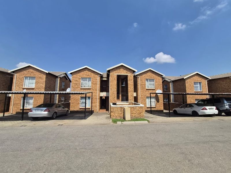 Front elevation of a multi-unit apartment complex featuring face brick construction, tiled roofing, and dedicated covered parking bays for residents.