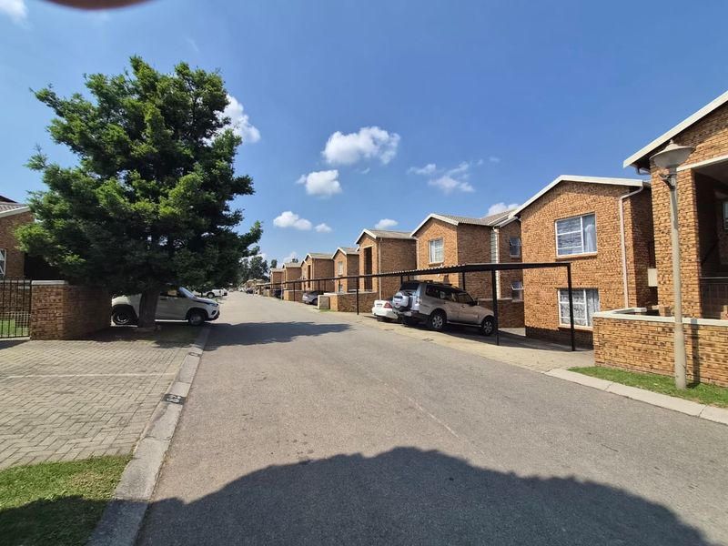 A view of the apartment complex street featuring brick buildings, paved driveways, and covered parking bays.