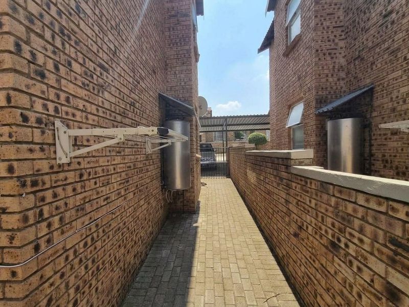 A narrow paved side passage between two face brick apartment buildings, featuring wall-mounted geysers and a drying rack.