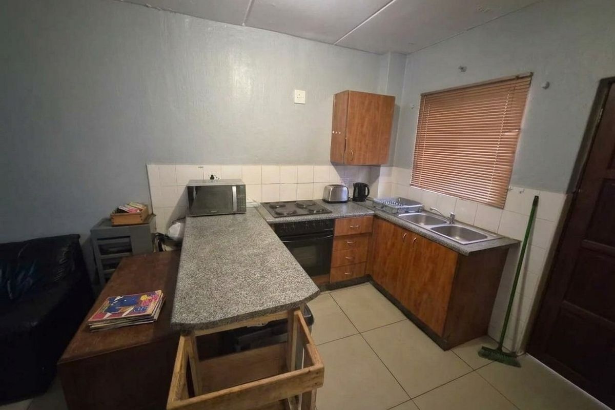 A compact kitchen featuring wood-finish cabinetry, laminate countertops, an integrated electric stove and oven, and a double basin sink with tiled backsplash.