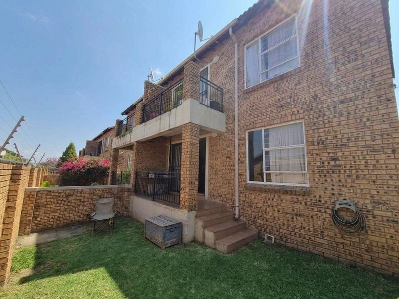 Rear view of a face brick apartment building featuring a ground floor patio, upper-level balcony with metal railings, and a private garden area.