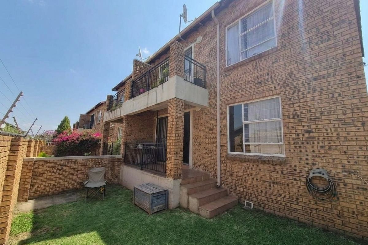 Rear view of a face brick apartment building featuring a ground floor patio, upper-level balcony with metal railings, and a private garden area.